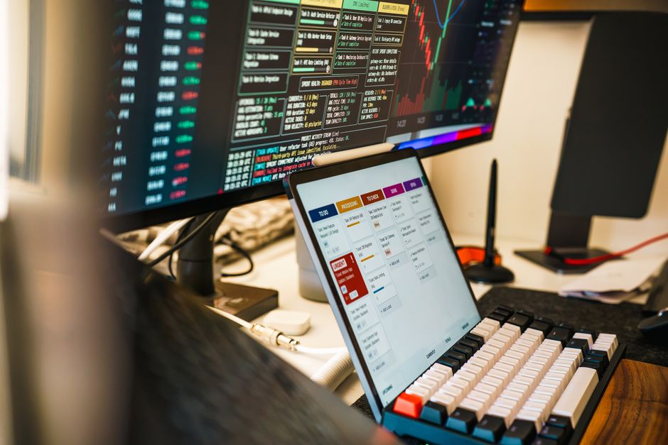 A sleek, modern workspace featuring trading monitors and a tablet for project management.